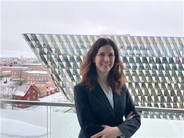 Porträtt av kvinna framför ett stort hus med glasfasad.