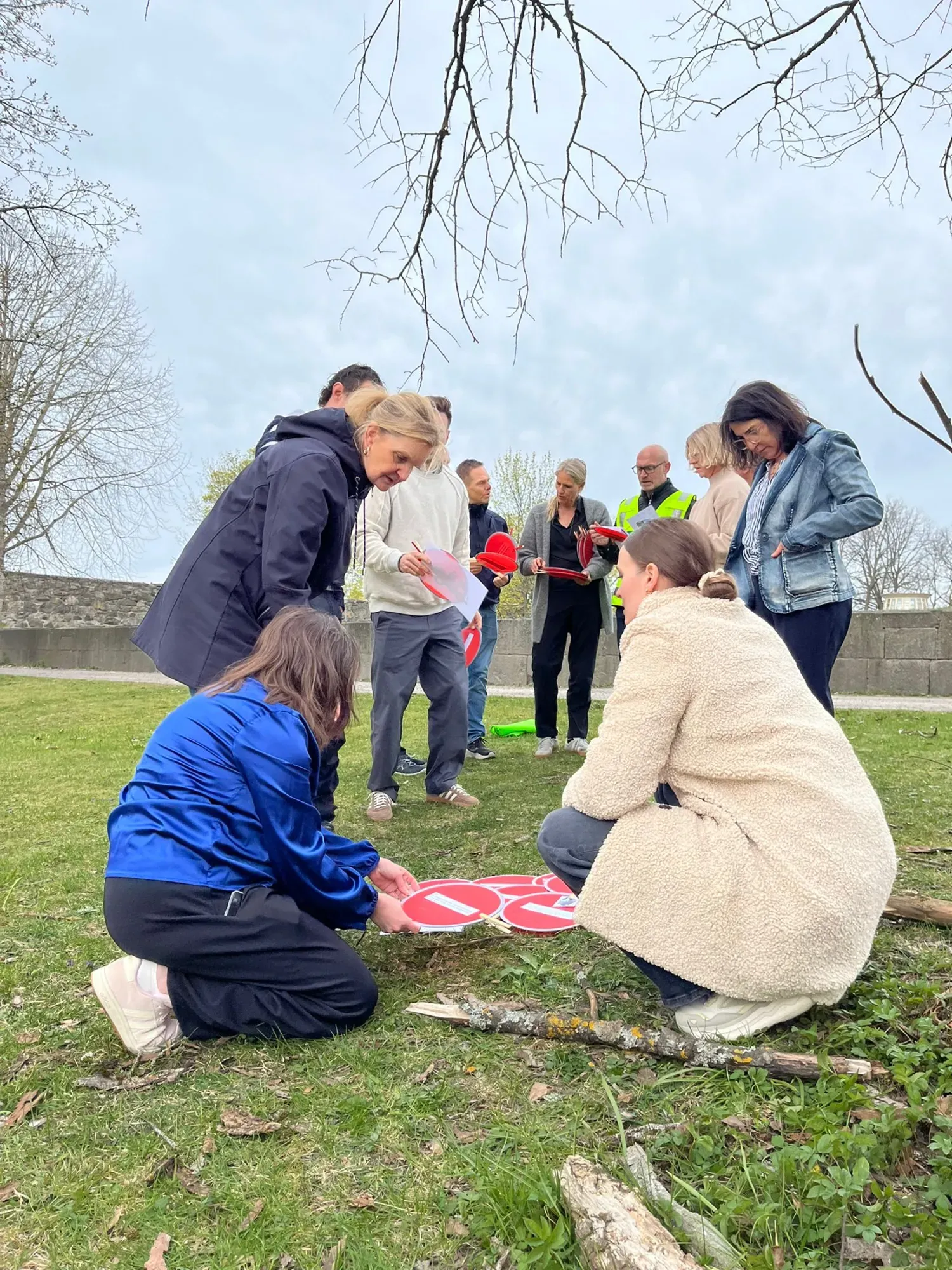 A group of people are standing on a grassy area, looking at small round discs. One person is wearing a high-visibility vest.