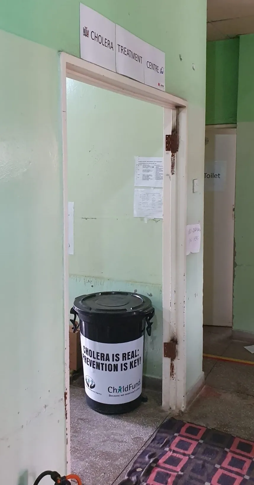 Entrance with a sign above that says cholera treatment centre. In the background you see a bucket