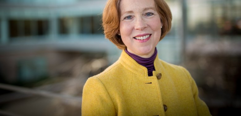 Portrait of Cynthia Bulik, she has red hair and a yellow jacket.