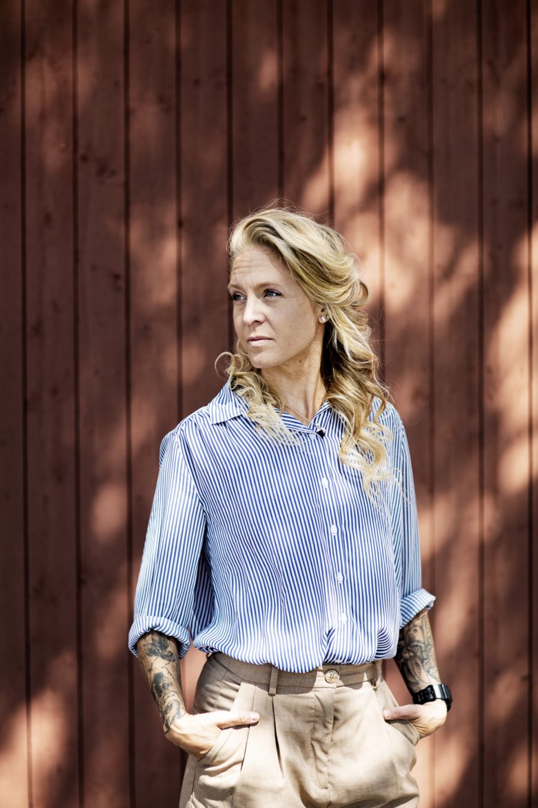 porträttbild av Elin Mohlin som står framför falurött trävägg ute.