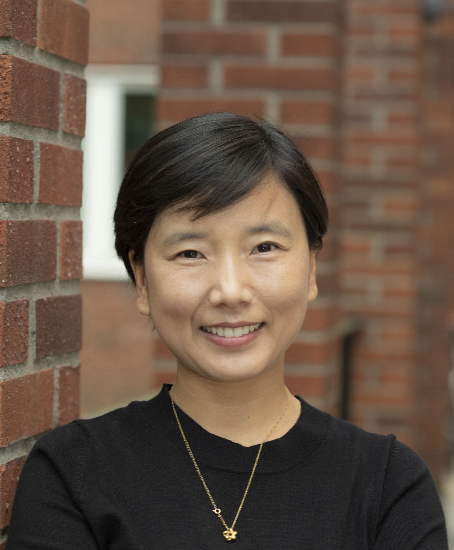 Portrait of Fang Fang in front of a brick wall.