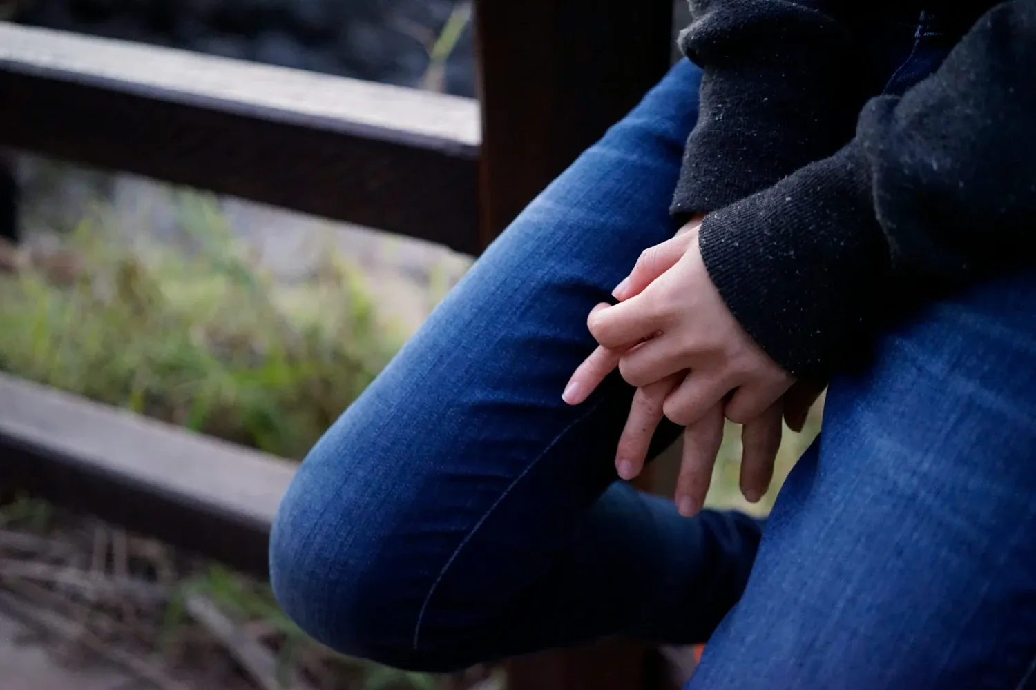 Person sitting on wooden fence wearing jeans and a blue sweather.