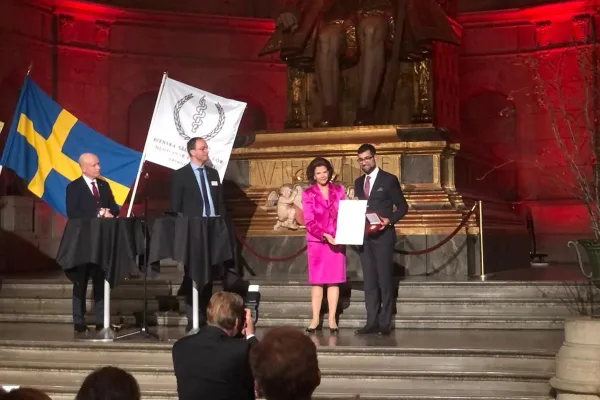 Queen Silivia hands the prize to Goncalo in front of a large statue of Gustav Vasa at the Nordic Museum in Stockholm.