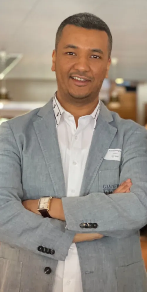 Portrait of a man, wearing a grey jacket, standing with his arms crossed.