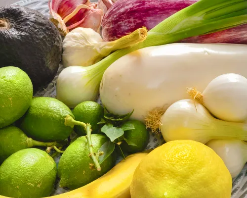 Close up of vibrant fruits and vegetables Including limes, lemon, eggplant, avocado, banana, garlic and scallions