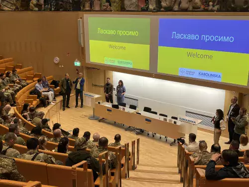 A hall full of people in uniforms, on screens at the front the Ukrainian flag is showing