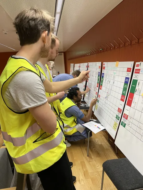 People in yellow high vis vests stranding looking at a whiteboard where rooms in a hospital has been drawn up