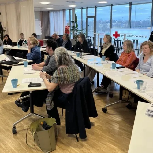 People are sitting in a classroom; in the background, there is a sign that says ‘Red Cross’ in Swedish and some windows overlooking the sea